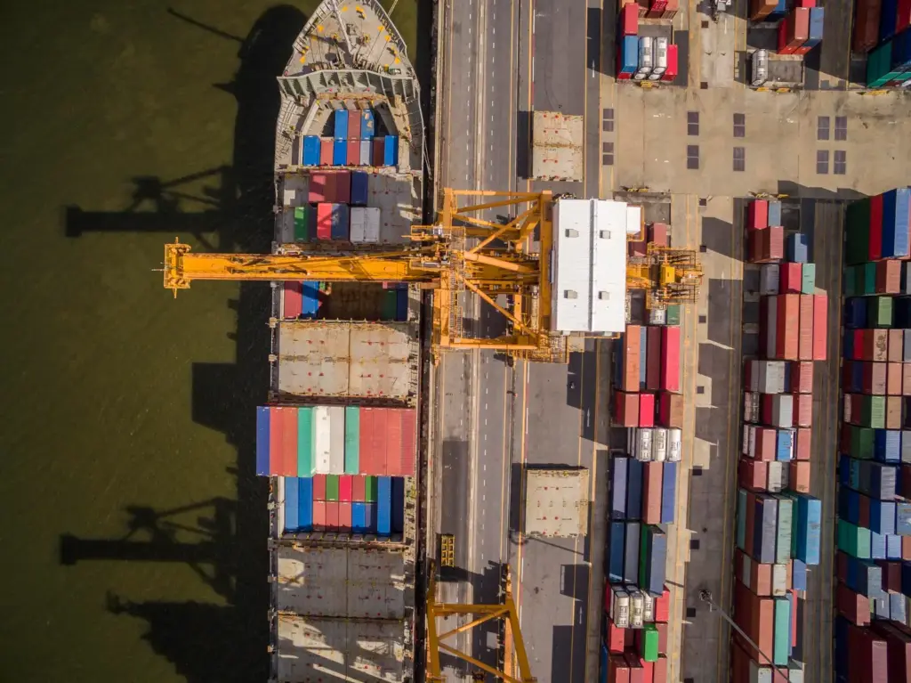 Vista aérea de porto com guindaste e contêineres coloridos, representando o fluxo de importação e a rastreabilidade logística no comércio exterior