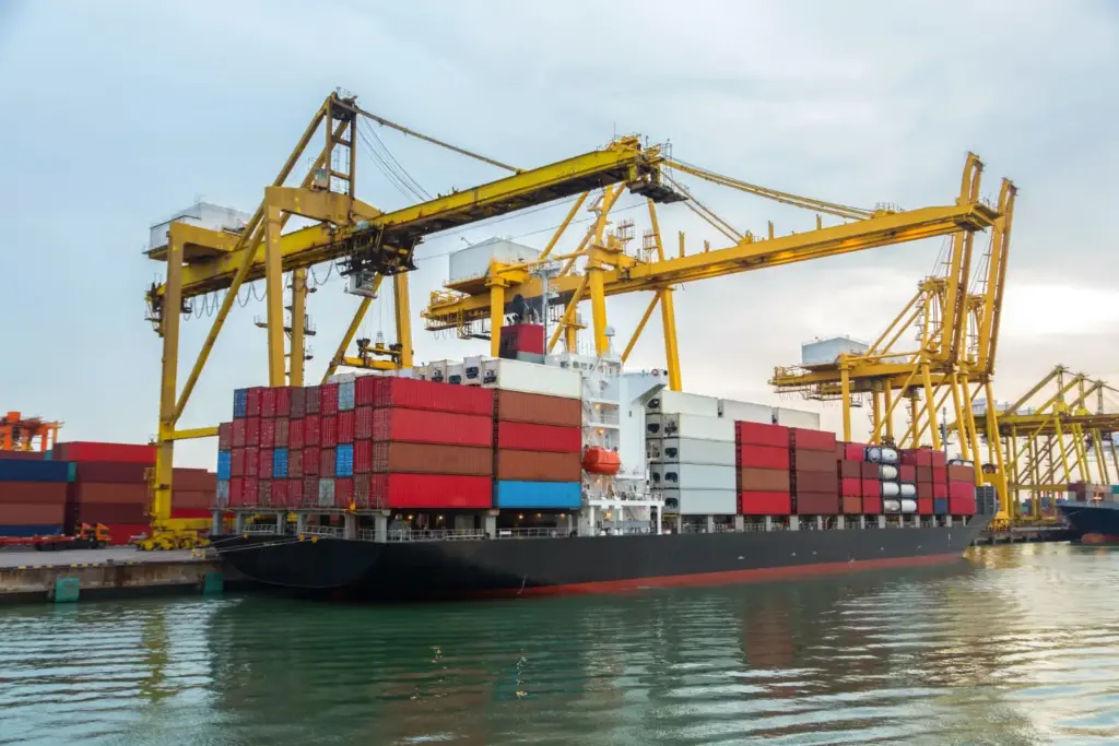 Navio porta-contêineres atracado com guindastes amarelos em porto, representando operações de importação sujeitas à DUIMP no comércio exterior